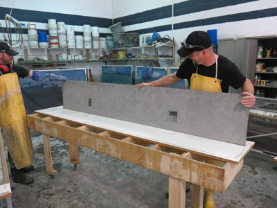 two men in yellow rubber aprons holding gray concrete backsplash in shop